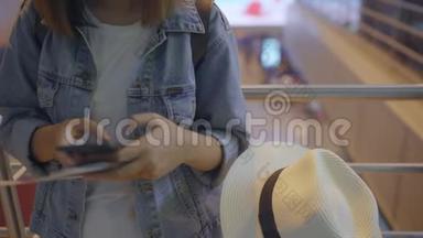 快乐的亚洲女人在机场<strong>登机</strong>口等待航班时，在候机大厅使用和检查她的智能手机。